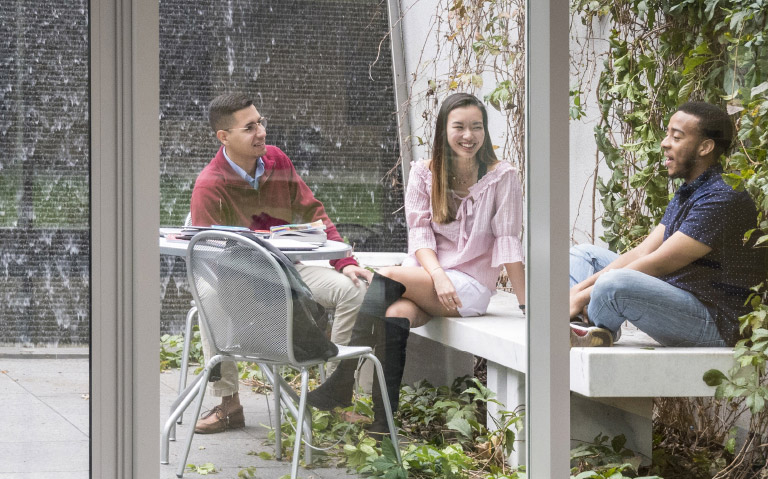 Three students sitting outside talking and laughing
