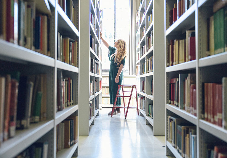 Student looking through books in library stacks