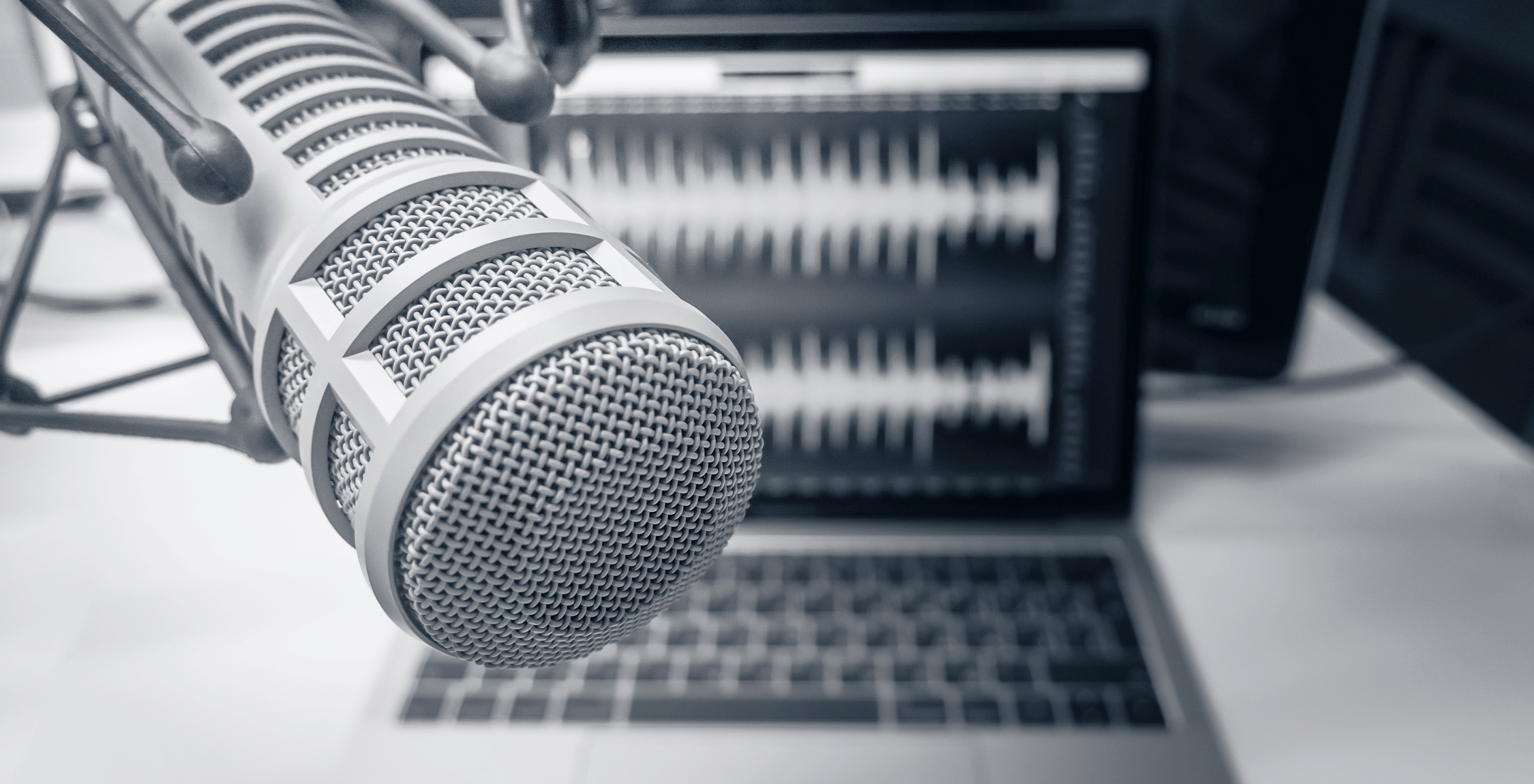 black and white photo of a recording studio microphone in front of a laptop displaying soundwaves